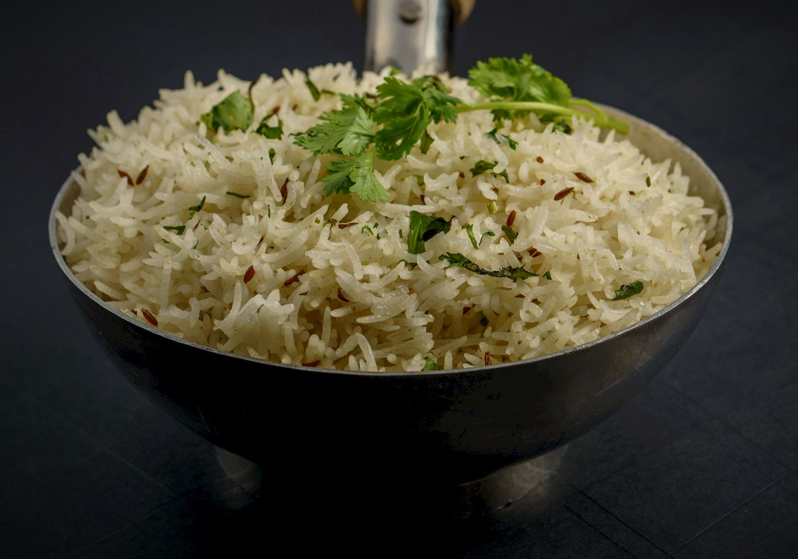 Cumin-flecked basmati rice with coriander in a steel bowl on dark slate