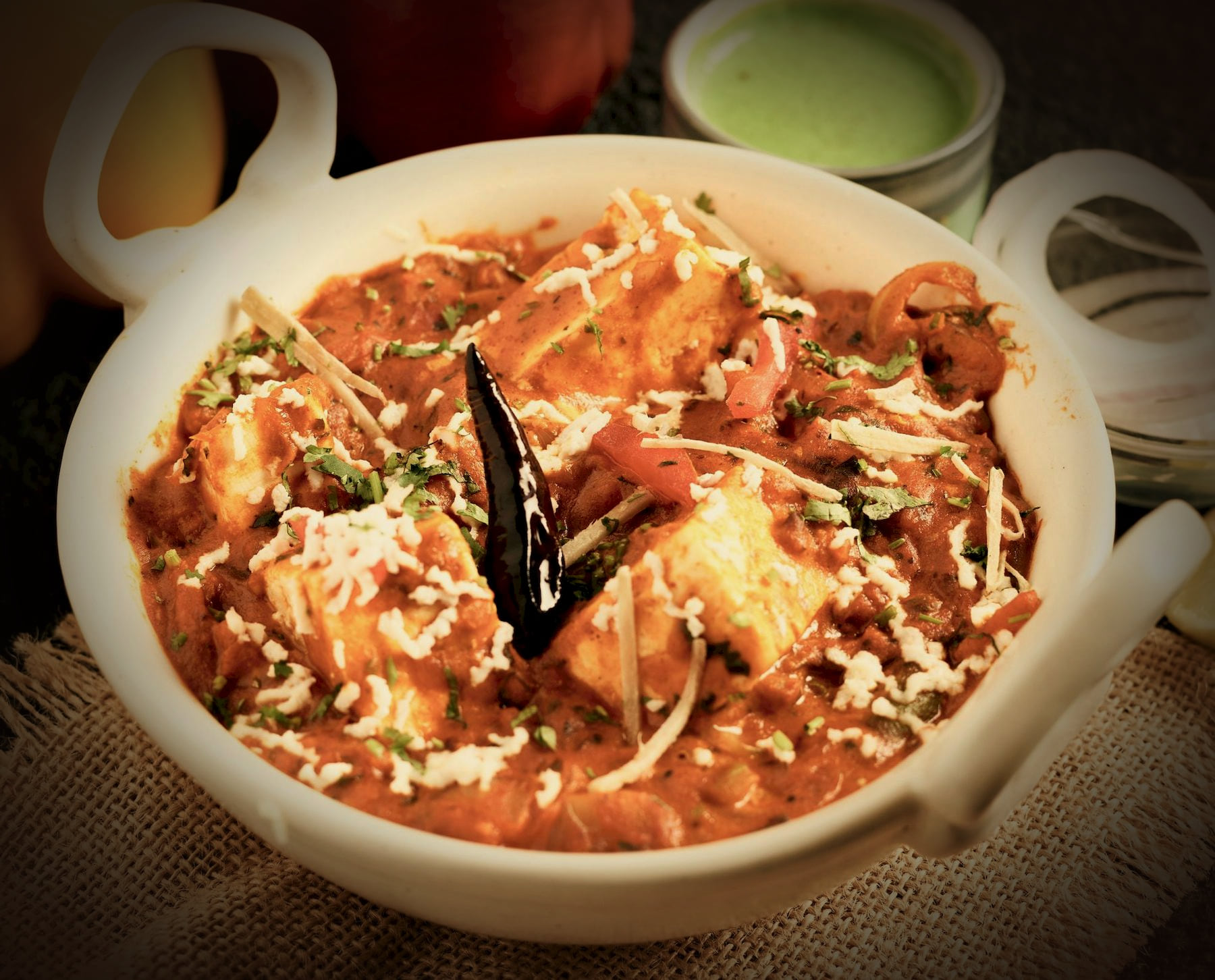 Paneer in a glossy orange-red masala in a handled ivory ceramic bowl
