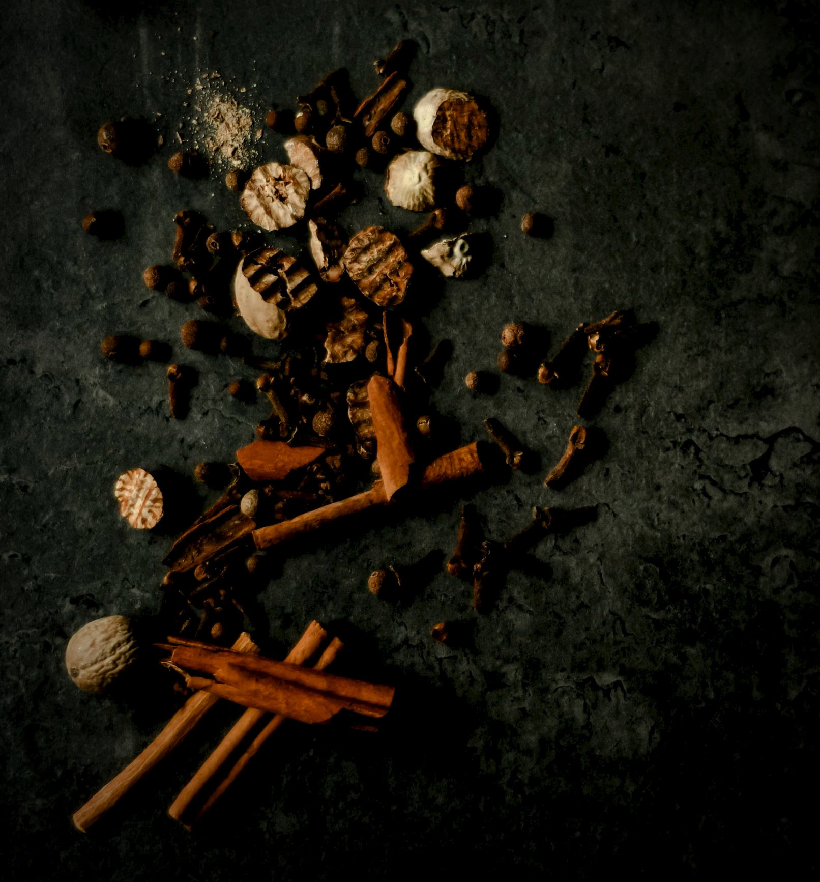 Whole mace, nutmeg, cinnamon and cloves on dark stone