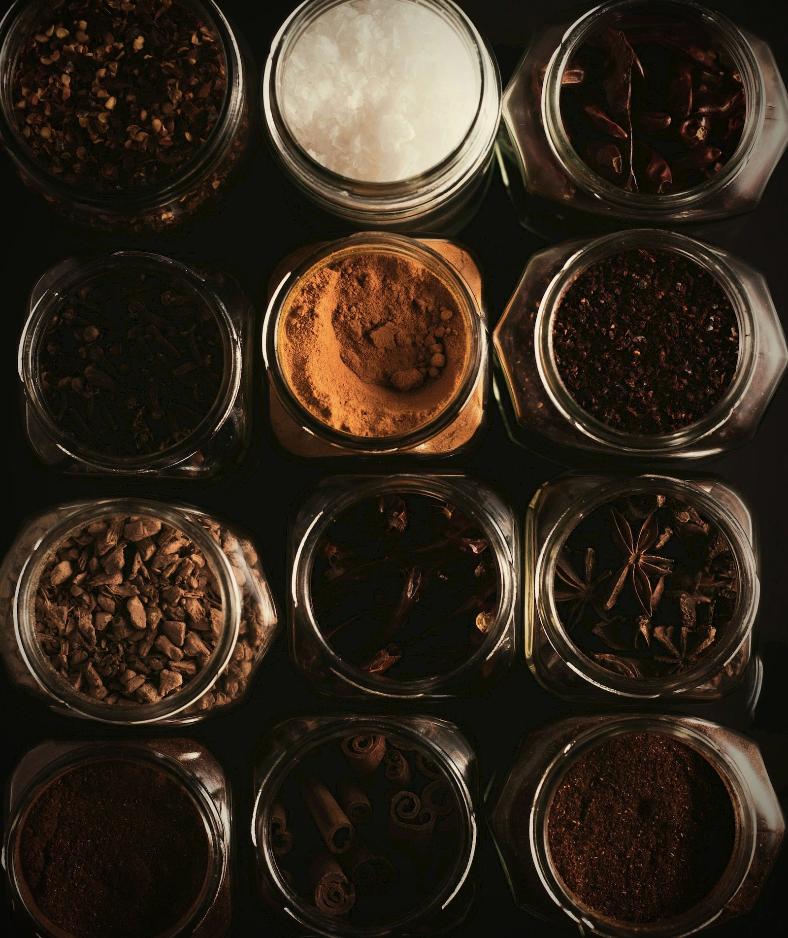 Whole and ground spices in glass jars, arranged in a grid