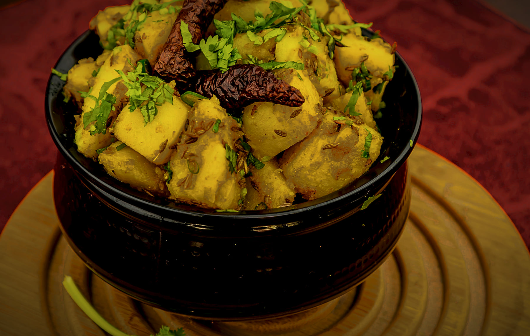 Potatoes coated in whole spices and dried red chillies in a dark hammered handi