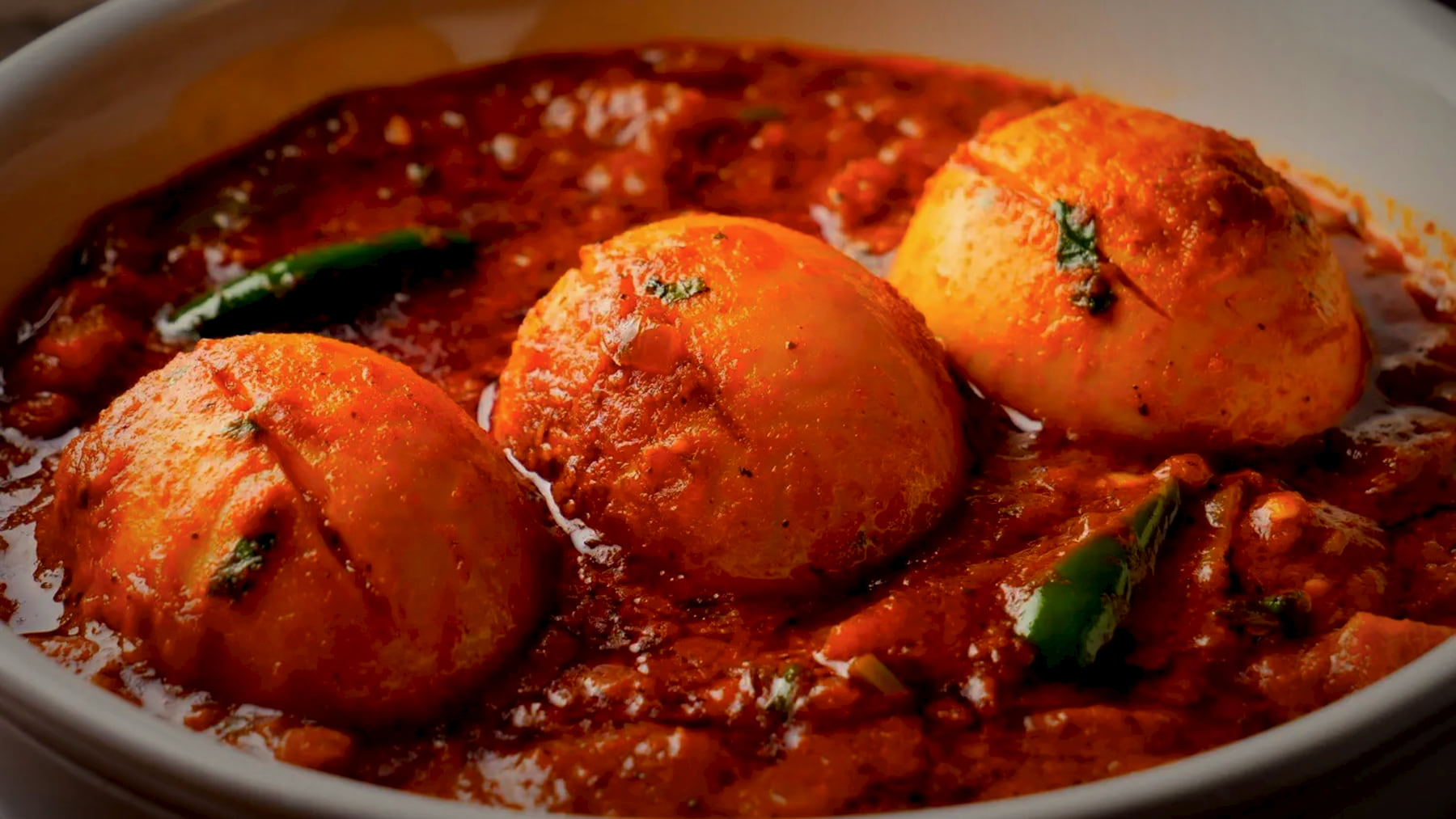 Three scored boiled eggs in a rich red masala with green chillies