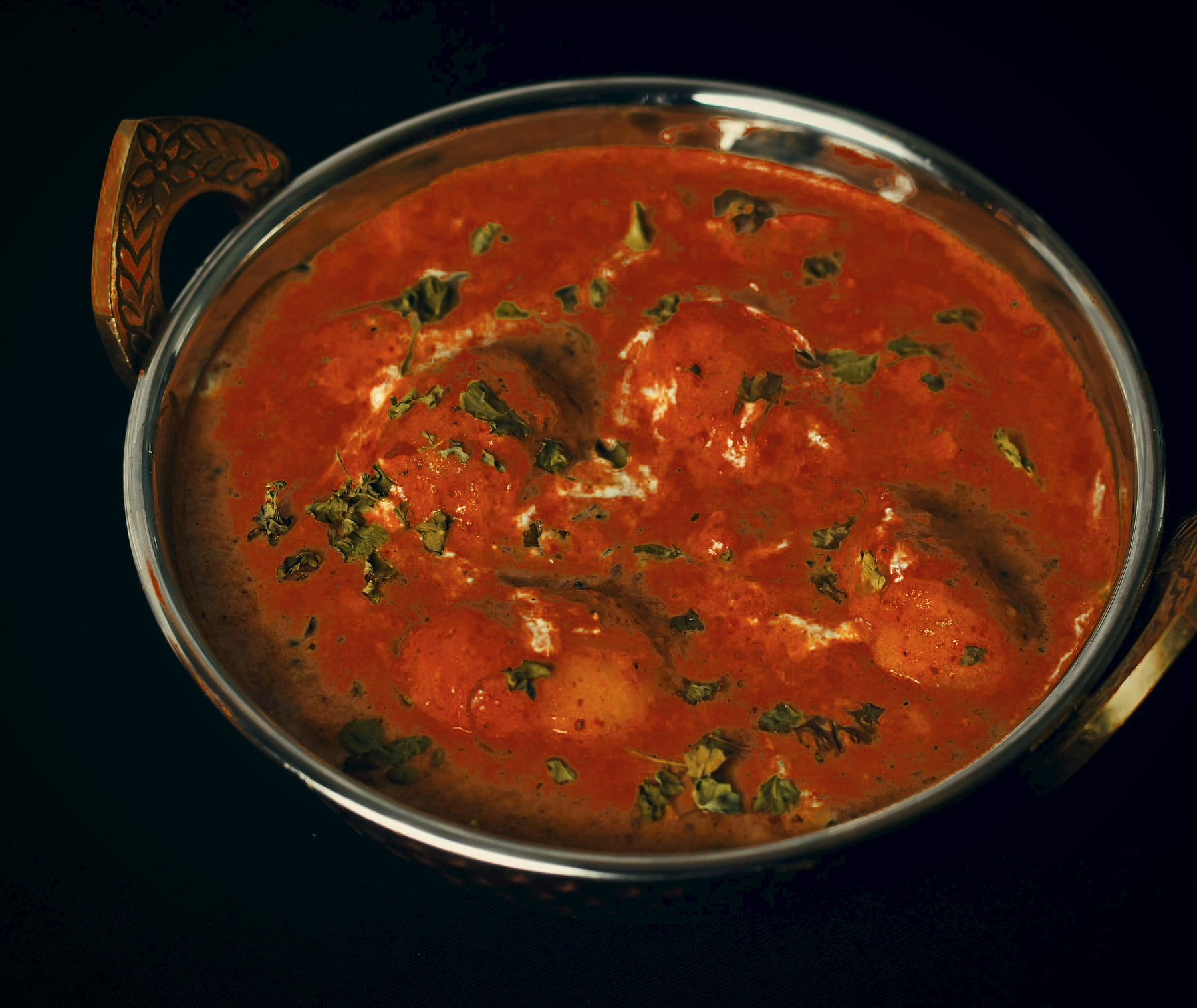 Whole small potatoes in a deep Kashmiri red gravy in a brass-handled kadai