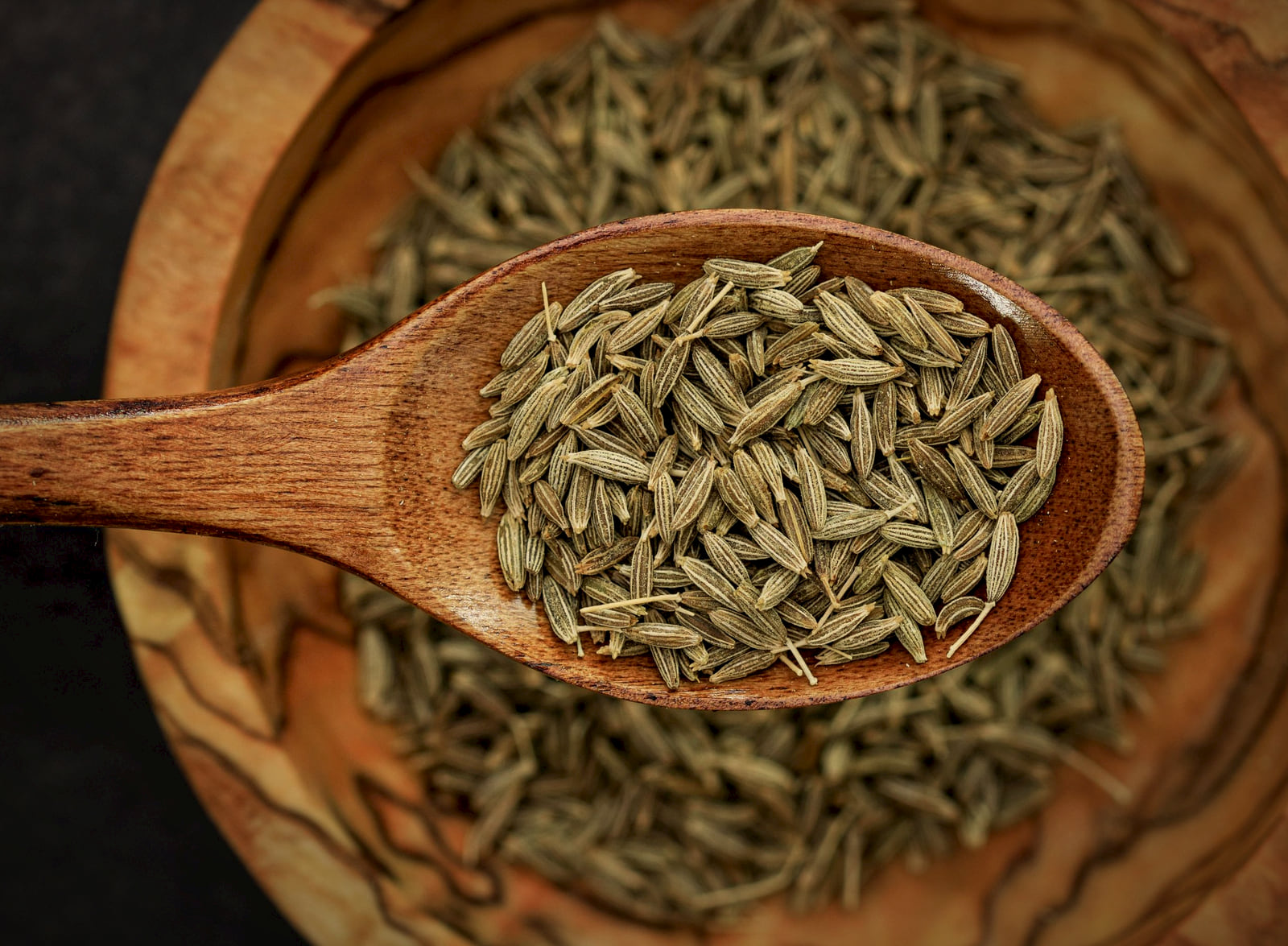 Cumin seeds heaped in a carved wooden spoon over a bowl of cumin